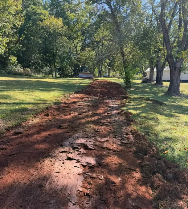 Red-clay drive cut through a lawn at the start of a house site