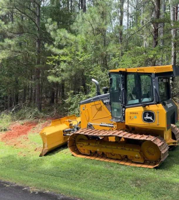 John Deere dozer parked beside a lot being cleared of pine trees
