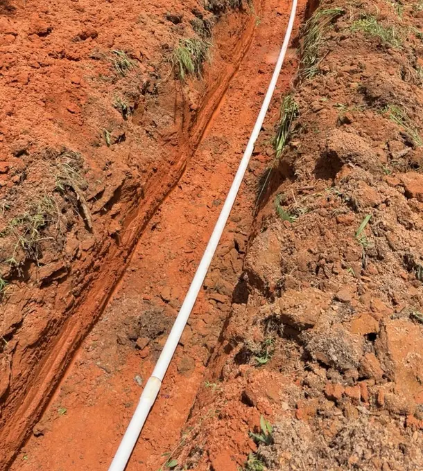 Water pipe laid in a red-clay trench beside a gravel drive
