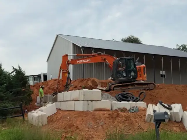 Excavator working beside a stacked block wall on a hillside property