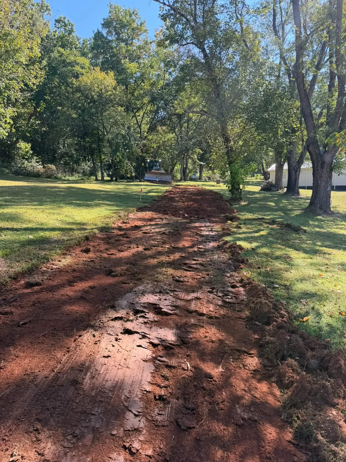 Red-clay drive cut through a lawn at the start of a house site
