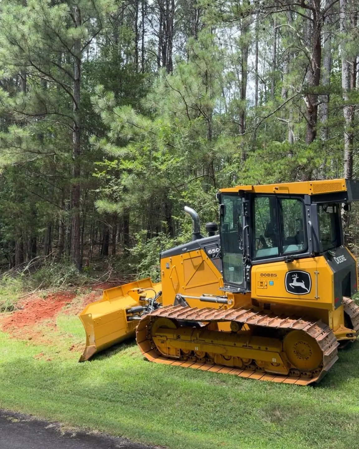 John Deere dozer parked beside a lot being cleared of pine trees