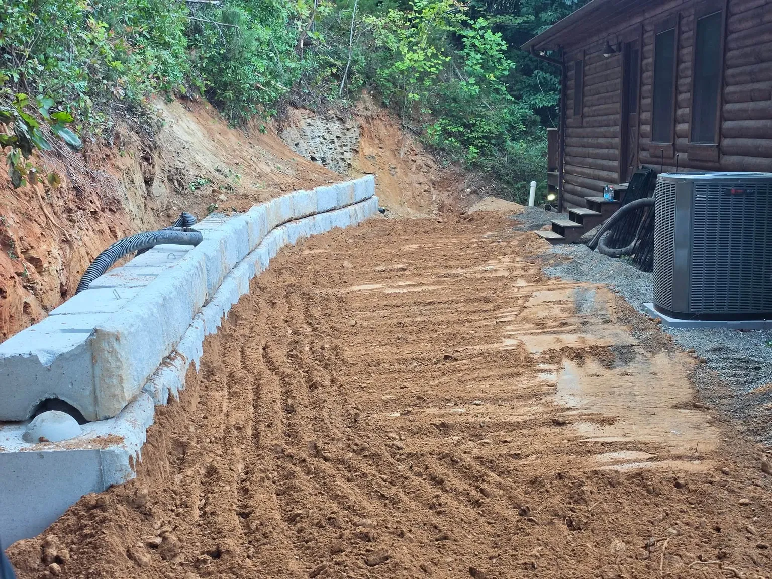Retaining wall blocks being set along a cut hillside beside a cabin