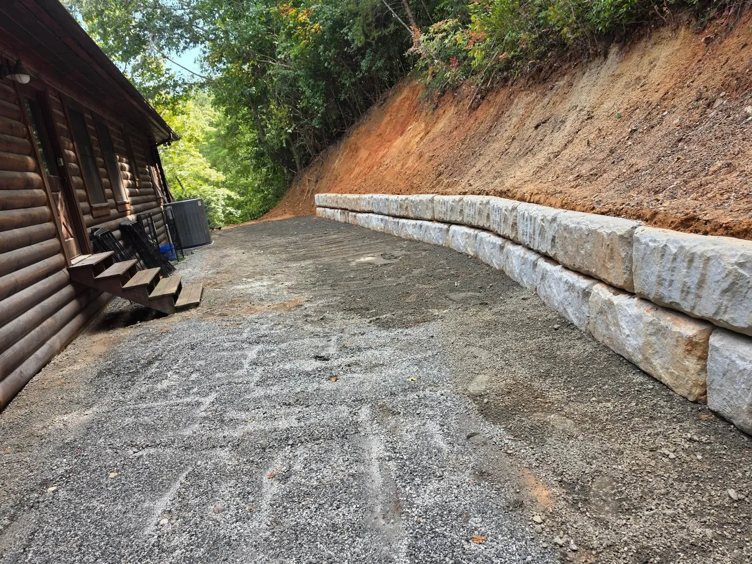 Finished block retaining wall and graded gravel drive beside a log cabin