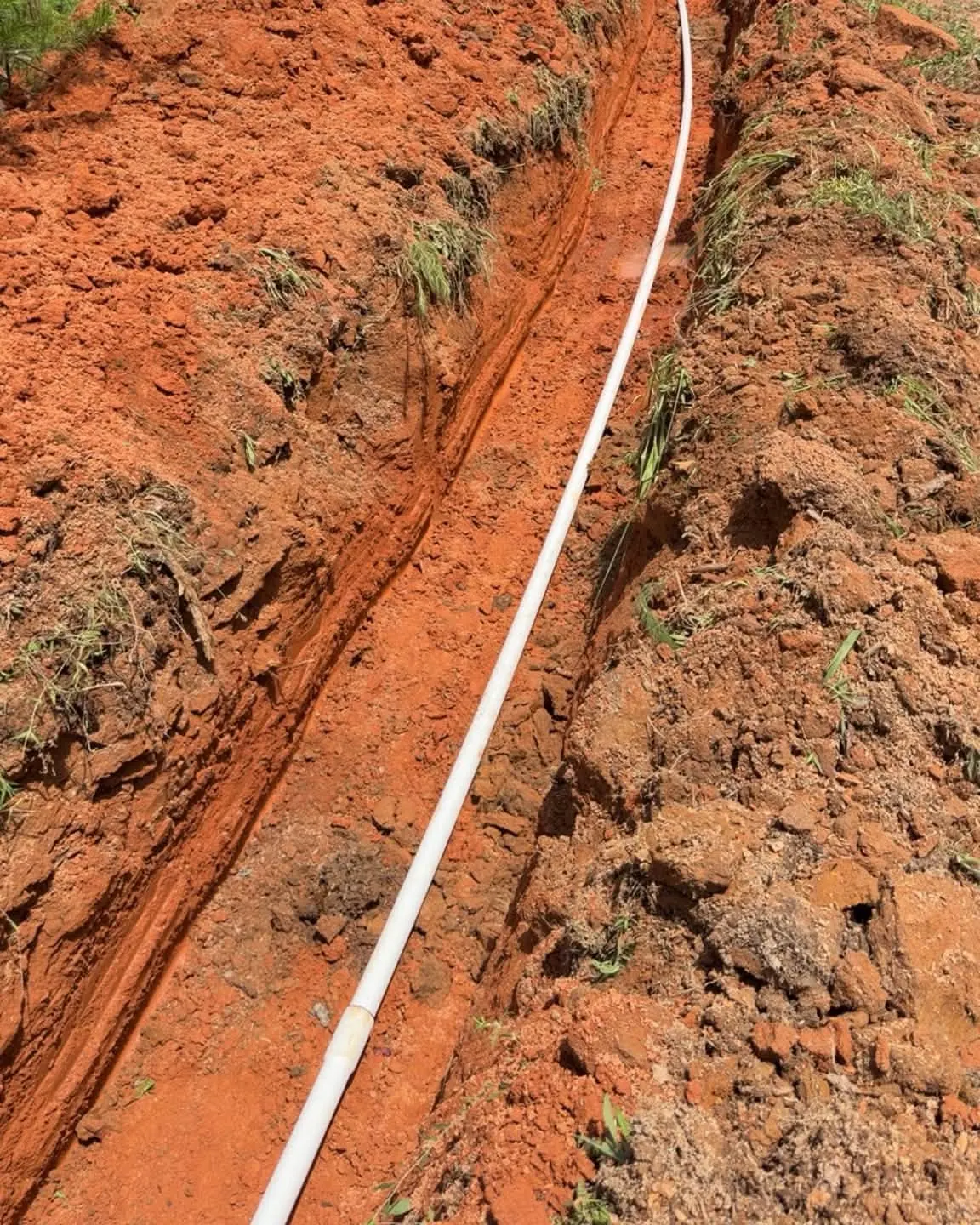 Water pipe laid in a red-clay trench beside a gravel drive